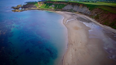 Aerial view of a serene coastal landscape with cliffs, a sandy beach, and clear blue waters.の写真素材