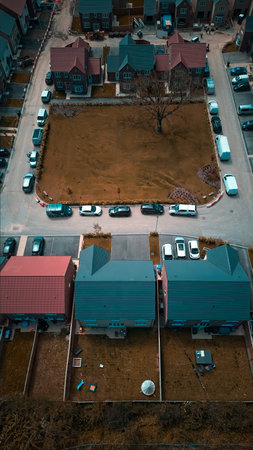 Aerial view of a residential neighborhood with houses, parked cars, and a central grassy area.