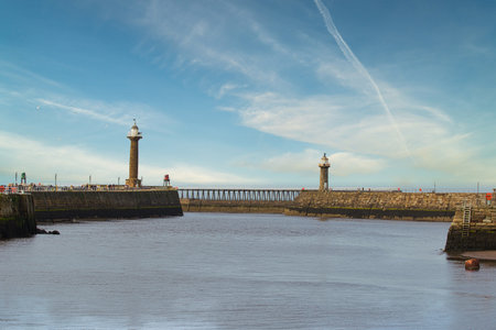 A serene harbor entrance with two lighthouses on either side, calm water, and a clear blue sky.の写真素材