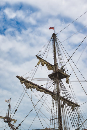 Tall ship masts with rigging and sails against a cloudy sky.の写真素材