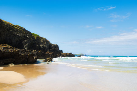 A serene beach scene featuring golden sand, gentle waves, and rocky cliffs under a clear blue sky. The tranquil atmosphere invites relaxation and enjoyment of nature's beauty.の写真素材