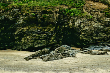 A rocky beach scene featuring rugged cliffs and smooth stones scattered on the sandy shore. The...