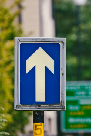 A blue road sign with a large white arrow pointing upwards, indicating straight ahead. The sign is...