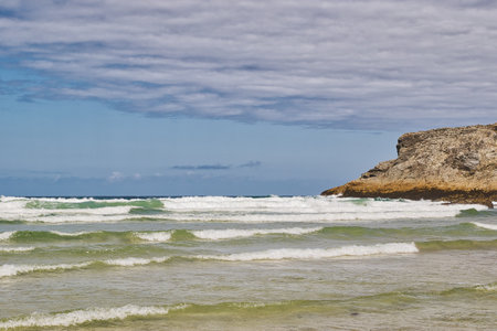 A serene beach scene featuring gentle waves lapping at the shore. The sky is partly cloudy with a...