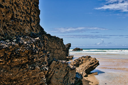 A scenic beach view featuring rugged rock formations and gentle waves. The rocks are textured and...
