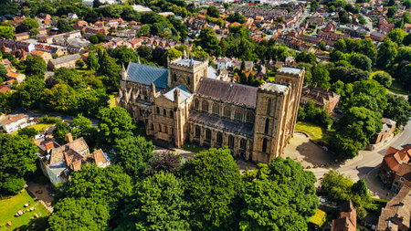 Aerial view of a large cathedral surrounded by lush green trees and a residential area. The cathedral features intricate architecture with tall towers and a beautiful roof. Nearby, there are houses and a park, showcasing a blend of nature and urban life.の写真素材