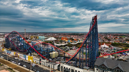 Aerial view of a vibrant amusement park featuring a large roller coaster with red and blue tracks. The park is bustling with activity, surrounded by various attractions and rides. The sky is overcast, adding a dramatic backdrop to the scene.の写真素材