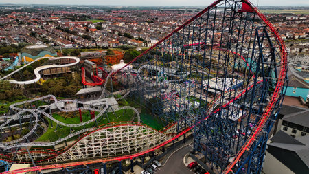 An aerial view of a vibrant amusement park featuring multiple roller coasters and rides. The scene showcases a large, red and blue roller coaster dominating the landscape, surrounded by various attractions and a residential area in the background.の写真素材