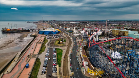 Aerial view of a coastal amusement park and beach area, featuring colorful rides, a pier, and a bustling seaside town. The sky is overcast, adding a dramatic effect to the scene.の写真素材