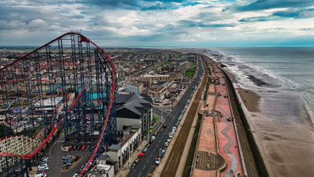 Aerial view of a coastal town featuring a large amusement park ride, sandy beach, and a promenade. The sky is partly cloudy, and the ocean waves are visible along the shore.の写真素材