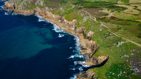 Aerial view of a rugged coastline with cliffs, green hills, and blue ocean waves crashing against...