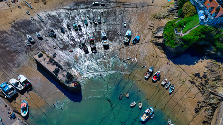 Aerial view of a harbor at low tide, showcasing numerous boats resting on the exposed mud. The water...