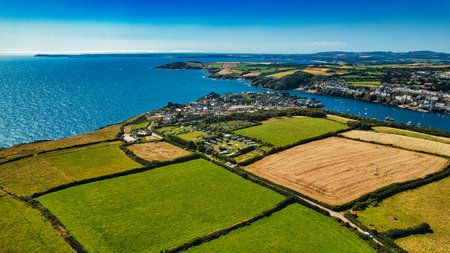 Aerial view of a coastal village surrounded by lush green fields and farmland. The blue sea stretches out in the background, with boats dotting the water. The landscape features a mix of agricultural land and residential areas, showcasing the beauty of rural life by the coast.の写真素材