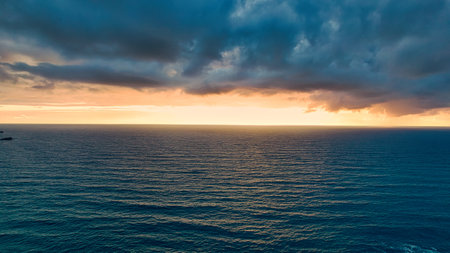 A serene seascape at sunset, showcasing a vast ocean under a dramatic sky filled with clouds. The...
