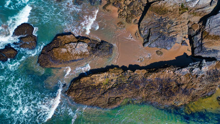 Aerial view of rocky coastline with waves crashing against the rocks. The sandy beach is visible...