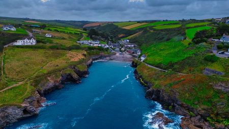 Aerial view of a coastal village surrounded by lush green hills and rocky shores. The turquoise water contrasts with the dark rocks and sandy beach. White houses dot the landscape, creating a picturesque scene of nature and tranquility.の写真素材
