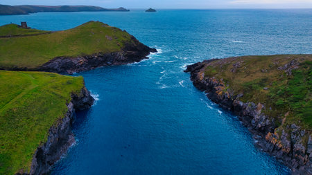 Aerial view of a serene coastal landscape featuring lush green hills and a calm blue sea. The water flows between two rocky formations, with distant islands visible on the horizon. The scene captures the beauty of nature and tranquility.の写真素材