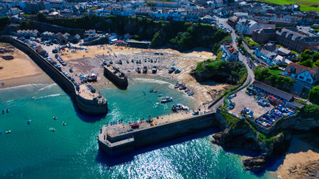 Aerial view of a coastal harbor with boats, sandy beach, and surrounding town. The harbor features...