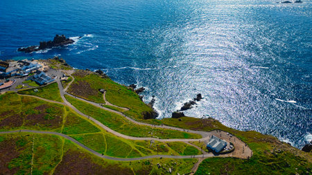 Aerial view of a coastal landscape featuring green hills, winding paths, and a sparkling blue ocean....