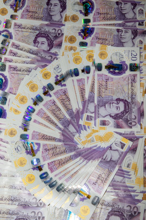 A fan of twenty-pound banknotes arranged in a spiral pattern, showcasing the intricate designs and colors of the currency. The notes feature a portrait of Queen Elizabeth II and holographic elements, emphasizing their security features.の写真素材