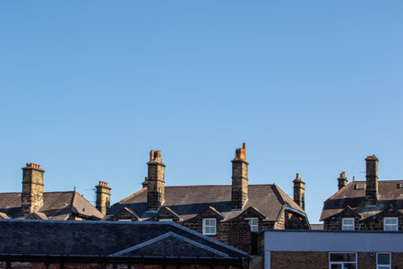 A clear blue sky above a row of traditional brick houses with multiple chimneys. The houses feature slate roofs and a mix of architectural styles, showcasing a charming urban landscape.の写真素材