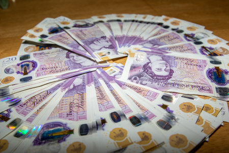 A circular arrangement of twenty-pound banknotes spread out on a wooden surface, showcasing the...