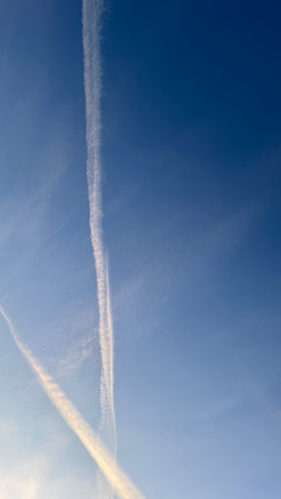 Two contrails, appearing as long, white streaks, are prominently featured against a clear, pale blue sky.  The contrails exhibit slight variations in thickness and density.の写真素材