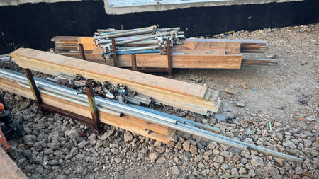 Construction materials, including wooden planks and metal pipes, are stacked on rusty metal racks outdoors on a gravel surface.  The scene appears to be a construction site.の写真素材
