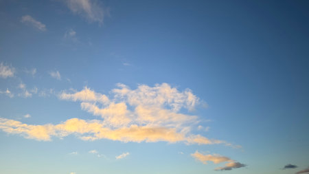 A mostly clear blue sky with a prominent band of pale yellow-white cirrus clouds stretching horizontally across the middle third.  Smaller, similar clouds are scattered throughout. The sky is a light blue, deepening in tone towards the upper portion.の写真素材