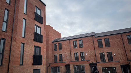 Red brick apartment buildings with black-framed windows and balconies. One building is taller than the row of attached townhouses. The sky is overcast.の写真素材