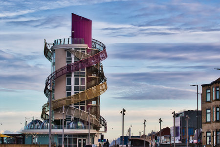 A multi-story building with a prominent spiral slide wraps around its exterior.  The structure features glass panels, a purple top section, and gold and maroon metalwork.  It's situated near other buildings under a partly cloudy sky in Redcar, UK.の写真素材