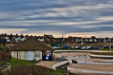 A seaside kiosk with a brown roof and light-colored walls sits near a parking lot and row of houses under a cloudy sky.  The scene appears calm and slightly overcast in Redcar, UK.の写真素材