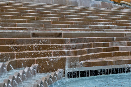 Stone steps cascading water into a pool.  Brown stone steps form a curved water feature, water flowing over the steps into a blue pool below in Birmingham, UK.の写真素材