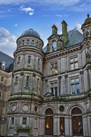 A grey stone building with a dome, multiple windows, and arched entrances. The building shows signs of age and weathering, with visible moss or lichen. The sky is partly cloudy in Birmingham, UK.の写真素材