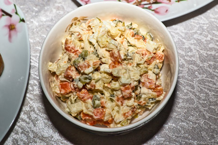 A bowl of creamy salad containing diced carrots, potatoes, eggs, and pickles.  The salad is in a white bowl on a light-colored tablecloth, Russian food.の写真素材