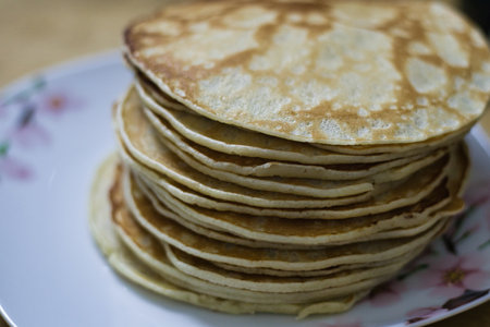 A tall stack of golden-brown pancakes sits on a floral-patterned plate.  The pancakes are neatly arranged, showing individual layers.  The plate is light blue and white.の写真素材