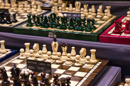 Multiple handmade chess sets displayed on a dark surface.  Sets feature various wood types and piece colors, including green, white, and red. Price tags are visible.の写真素材