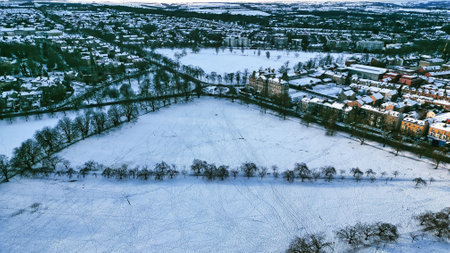 Aerial view of a snow-covered park bordered by residential buildings and trees.  The park shows...