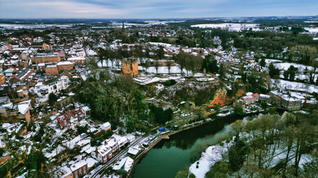 Aerial view of a snow-covered town with a castle ruin and river. Buildings are densely packed, with a mix of architectural styles.  Trees and snow-covered landscape surround the town in Knaresborough, UK.の写真素材