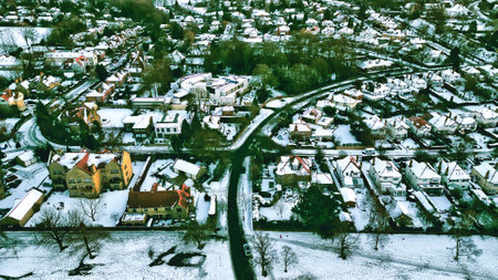 Aerial view of a snow-covered residential area, featuring various house styles, roads, and green spaces. A large building is centrally located. The overall color palette is muted with whites and greens dominating  in Harrogate, UK.の写真素材