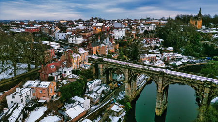 Aerial view of a snow-covered town with a stone viaduct spanning a river.  Buildings are densely packed, showing a mix of architectural styles.  Trees and a church spire are visible in the background in Knaresborough, UK.の写真素材