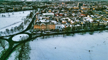 Aerial view of a snow-covered residential area near a park, featuring a large hotel and a roundabout. Buildings are predominantly light-colored, contrasting with the white snow and dark green trees  in Harrogate, UK.の写真素材