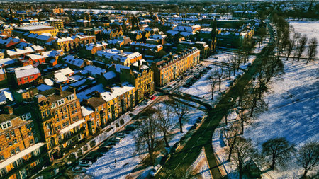 Aerial view of a snow-covered town with rows of houses, tree-lined streets, and a park, showcasing a mix of architectural styles and urban landscape features under winter sunlight  in Harrogate, UK.の写真素材