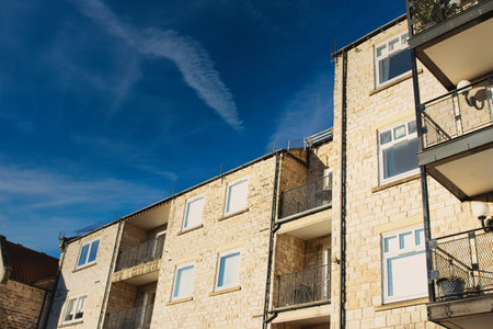 Low-angle view of a light beige stone apartment building with multiple balconies and windows under a clear blue sky.  The building displays a consistent architectural style in Wetherby, UK.の写真素材