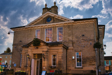 A tan stone building with a clock in the pediment, multiple windows, and decorative metalwork.  A black wrought iron fence is visible in the foreground. The building has a classical architectural style in Wetherby, UK.の写真素材