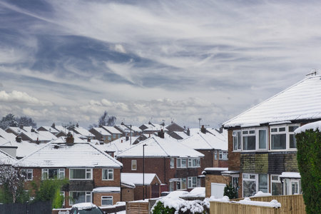 Snow-covered suburban houses under a cloudy sky.  Brick houses with snow on their roofs and window sills.  A residential street scene in winter in Harrogate, UK.の写真素材
