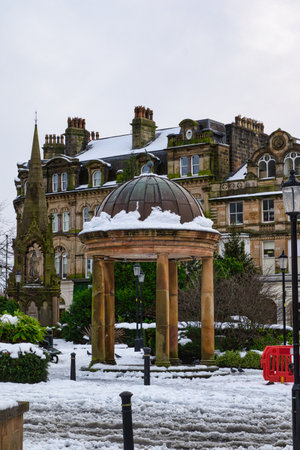 Snow-covered gazebo in front of a snow-dusted stone building.  Lampposts and a red barrier are visible.  The scene is peaceful and wintery in Harrogate, UK.の写真素材