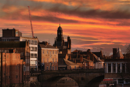 Urban landscape featuring brick buildings and a stone bridge under a dramatic orange and brown sky. Construction crane visible in York, UK.の写真素材