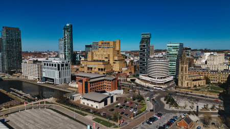 An aerial view of a city skyline under a clear blue sky features modern buildings and a historic church, with a canal and parking areas visible in Liverpool, UK.の写真素材