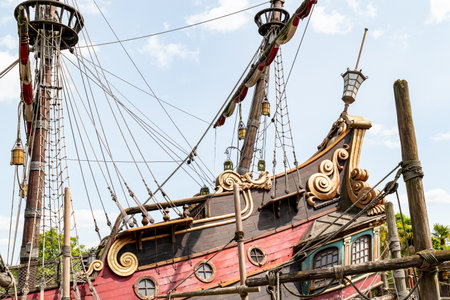 Low-angle shot of a pirate ship facade. Red and black wood with golden scrollwork, masts, rigging, and lantern details under a bright sky.の写真素材